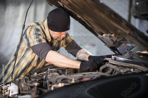 Car service. Brutal mechanic man standing by the car with open hood and checks the state