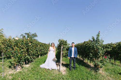 Happy young beautiful couple in blue clothes walking in the garden in sunny day. Couple in love smiling  hugging and kissing on the background of beautiful vineyard in Italy