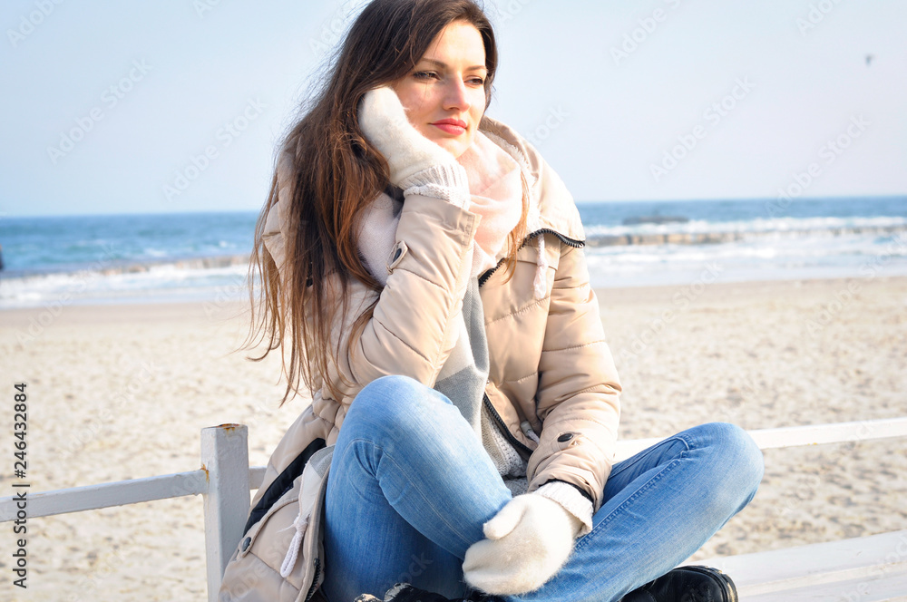 Young beautiful woman is sad, sitting on a bench alone at sea and looking into the distance.