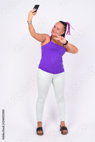 Full body shot of happy rebellious woman with dreadlocks taking selfie