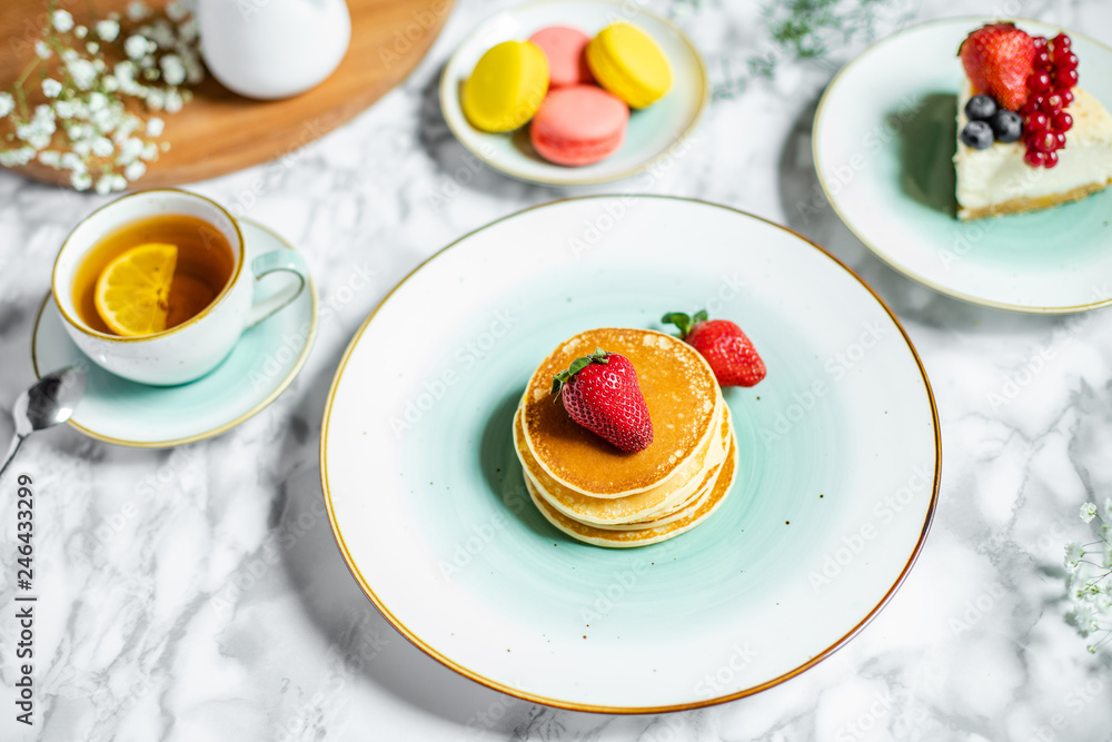 pancakes with tea, cheesecake and biscuits on a marble table with flowers pancakes with tea, cheesecake and biscuits on a marble table with flowers
