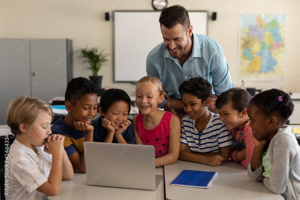 Male teacher teaching kids on laptop in classroom Male teacher teaching kids on laptop in classroom