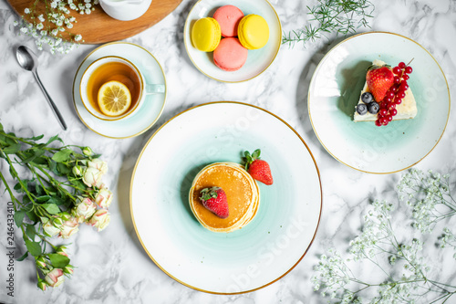 pancakes with tea, cheesecake and biscuits on a marble table with flowers