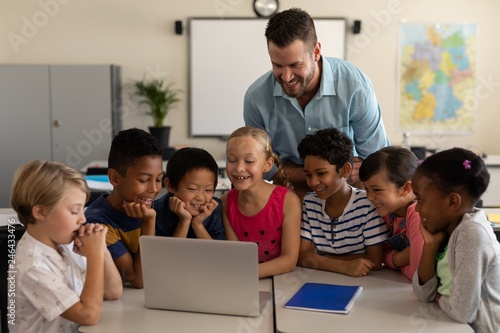 Male teacher teaching kids on laptop in classroom photo