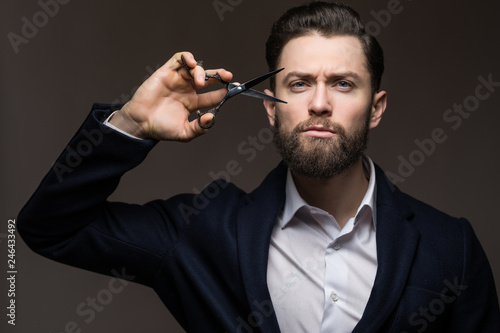 Barber scissors, barber shop. Young brarded brutal male hipster with moustache holding scissors near his face. Male in barbershop, haircut, shaving. Mans haircut in barber shop