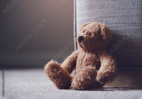 Teddy bear is laying down on carpet in retro filter, Lonely teddy bear laying down alone in living room at night ,lonely concept, international missing children's day. photo