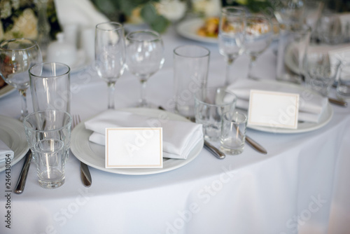 White dishes on the wedding table with empty cards. Wedding decoration in the rastaurant © WellStock
