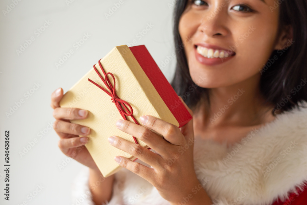 Joyful girl in Christmas dress showing gift with red bow. Beautiful brunette woman holding Christmas present box with copy space on top. Advertising concept