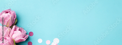 Pink tulip flowers on blue background decorated with confetti. Top view, flat lay.
