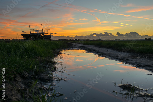 Sunset over the dutch countryside with reflections in a pool. Agricultural machinery stands in the farmland.
