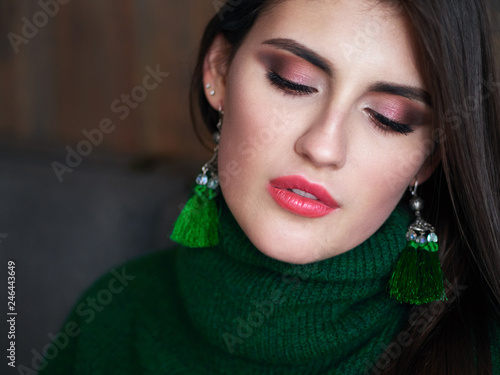 Casual portrait of happy young brunette woman with trendy makeup green sweater and brush earrings.