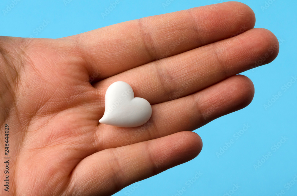 Hand holding a little white heart against blue background Hand holding a little white heart against blue background