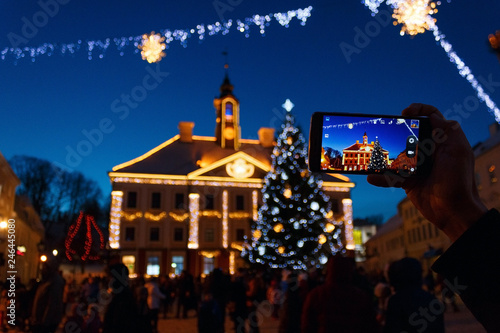Hand of a man who take a photo of Tartu Town Hall and Christmas tree on his smartphone during the Christmas celebrations. Tartu, Estonia.