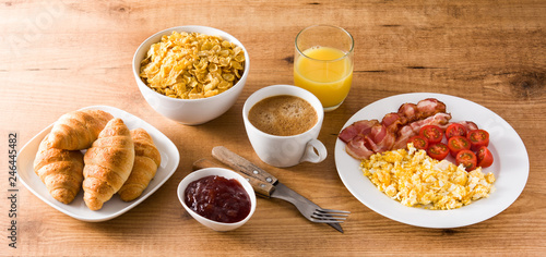 Breakfast with scrambled eggs, bacon, tomatoes,coffee,orange juice ,croissant and corn flakes on wooden table. Panoramic view