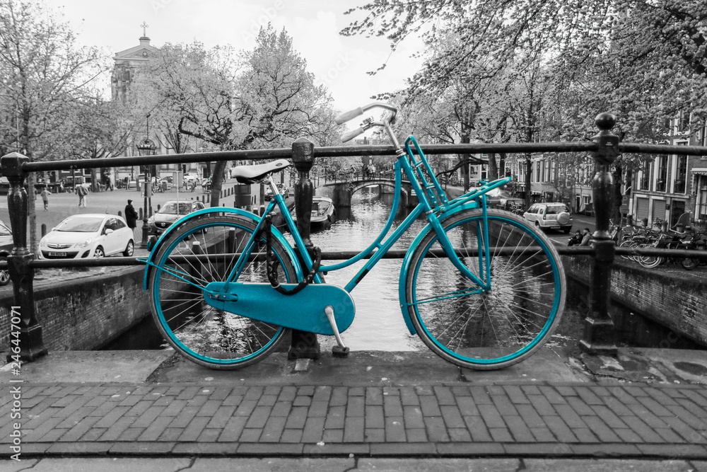 A picture of a lonely azure bike on the bridge over the channel in Amsterdam. The background is black and white. 