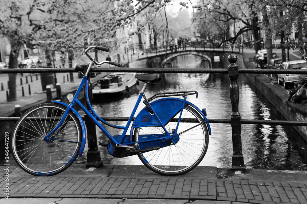 A picture of a lonely blue bike on the bridge over the channel in Amsterdam. The background is black and white. 