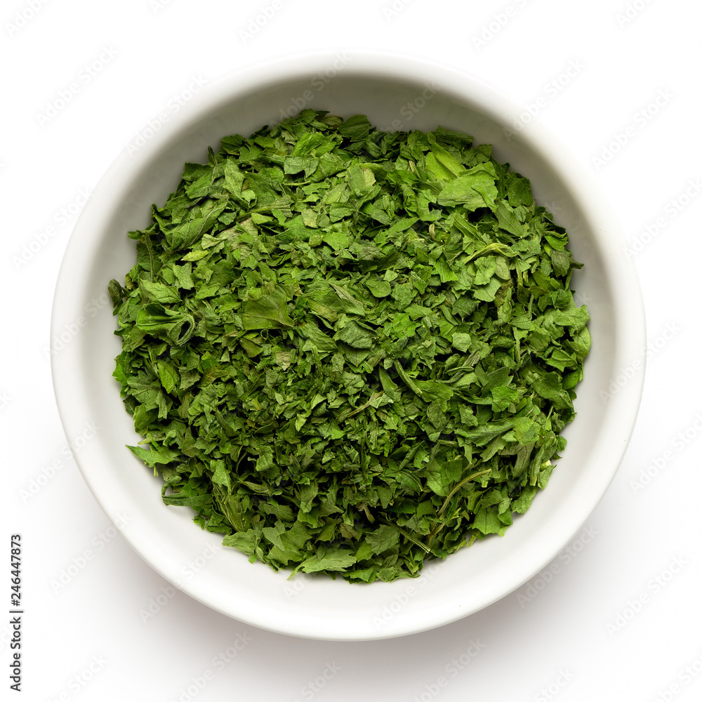 Dried chopped parsley in white ceramic bowl isolated on white from above. Dried chopped parsley in white ceramic bowl isolated on white from above.