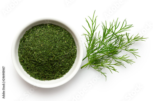 Photo Dried chopped dill in white ceramic bowl next to fresh dill leaves isolated on white from above