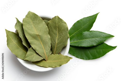 Dried bay leaves in white ceramic bowl next to fresh bay leaves isolated on white from above.