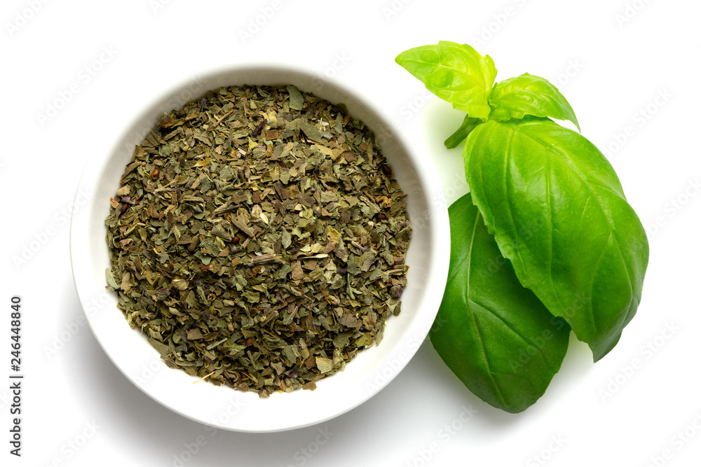 Dried chopped basil in white ceramic bowl next to fresh basil leaves isolated on white from above. Dried chopped basil in white ceramic bowl next to fresh basil leaves isolated on white from above.