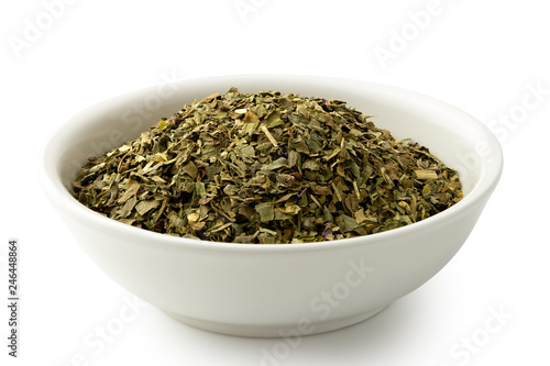 Dried chopped basil in white ceramic bowl isolated on white.