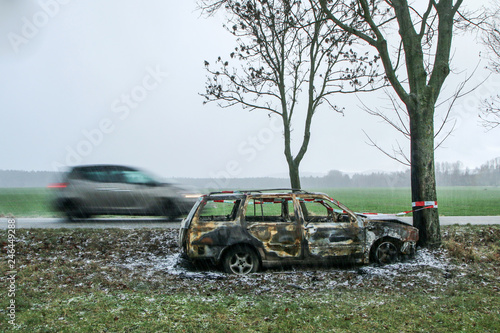 Fototapeta Naklejka Na Ścianę i Meble -  Car destroyed during the traffic accident. It was caused by the bad weather conditions in winter, because of the black ice or snow. The car is burnt, abandoned and stands by the road in the snowfall.
