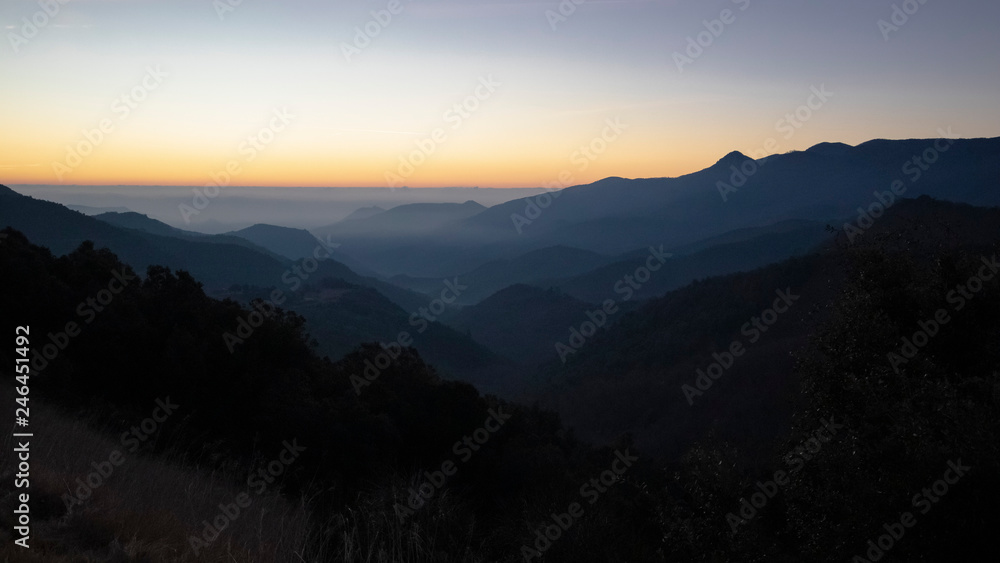 Sun rising on a foggy dark mountain range silhouette in Catalan Pyrenees