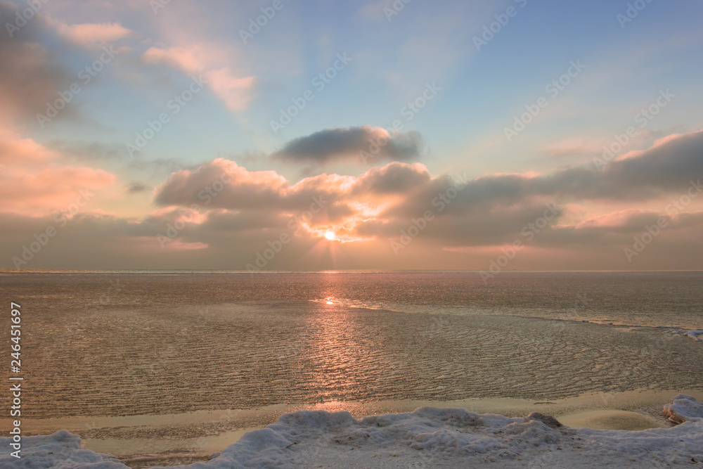 Obraz premium Setting sun among the clouds over the frozen sea in winter