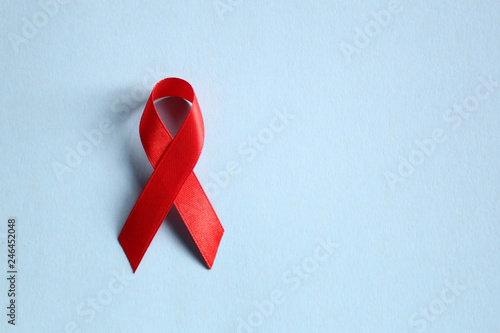 Obraz na plátně Red ribbon as symbol of aids awareness on blue  background