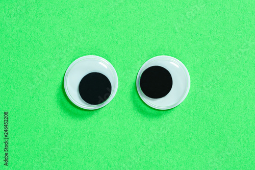 Mad googly eyes on neon green background. Cross-eyed funny toys eyes close up.