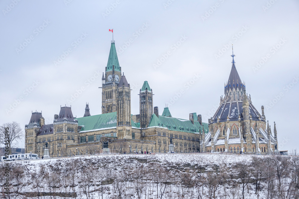 Scenic view of parliament of Canada building on bank of Ottawa river in Ontario in capital of country. Depressive beautiful winter look of old historic famous government building covered by snow