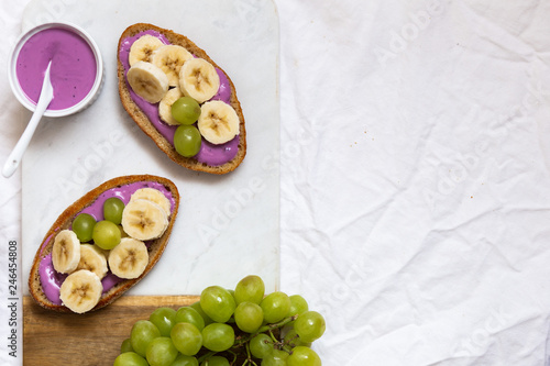 bread dessert sandwiches with yogurt and banana on a rustic cutting board with grapes on white background, top view. Flat lay. Delicious breakfast or snack