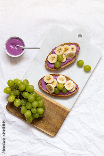 bread dessert sandwiches with yogurt and banana on a rustic cutting board with grapes on white background, top view. Flat lay. Delicious breakfast or snack