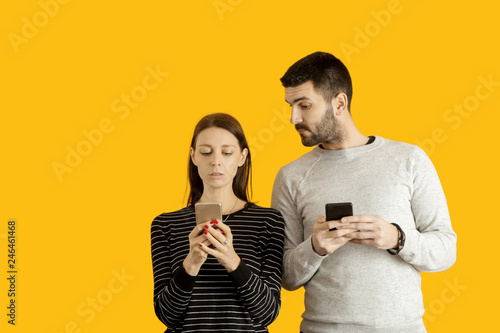 Fényképezés Young man and woman are typing on their mobile phones, studio portrait on the yellow background