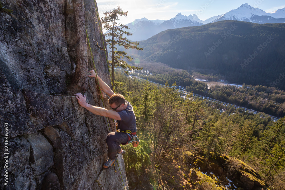 Male Rock climber climbing on the edge of the cliff during a sunny winter sunset. Taken in Area 44 near Squamish and Whistler, North of Vancouver, BC, Canada. Male Rock climber climbing on the edge of the cliff during a sunny winter sunset. Taken in Area 44 near Squamish and Whistler, North of Vancouver, BC, Canada.