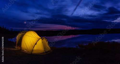 Lit Tent in nature near a calm lake during a vibrant sunset. Taken in Northern Newfoundland, Canada.
