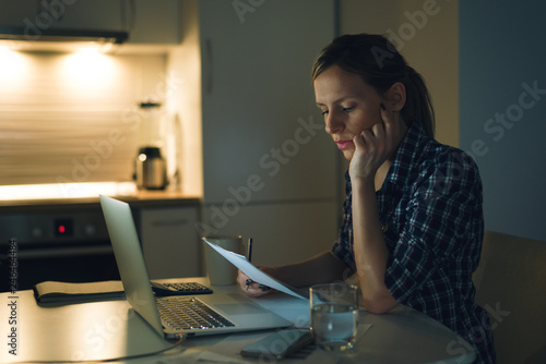 Serious woman reading her financial bills at home