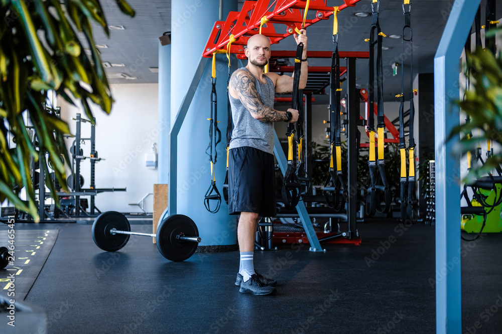 Φωτογραφία Tattooed athletic man holding a suspension fitness rope