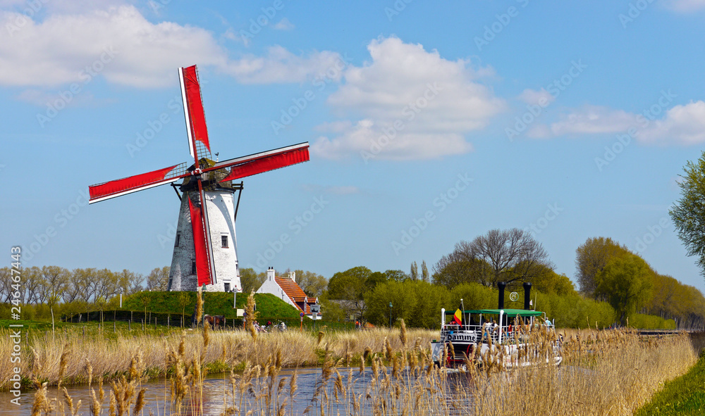 Obraz premium Damme, West Flanders / Belgium - May 2013: A tourist boat crossing the canal between Brugges and Damme, with a windmill in the background