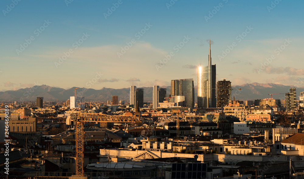 Milan (Italy) skyline at sunset with modern skyscrapers in Porta Nuova business district. Panoramic view of Milano city. The mountain range of the Lombardy Alps in the background.