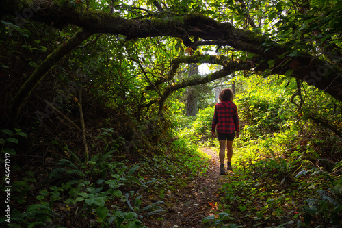 Woman walking through the green rain forest during a vibrant summer day. Taken in Northern Vancouver Island, BC, Canada.