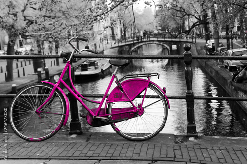 A picture of a lonely pink bike on the bridge over the channel in Amsterdam. The background is black and white. 