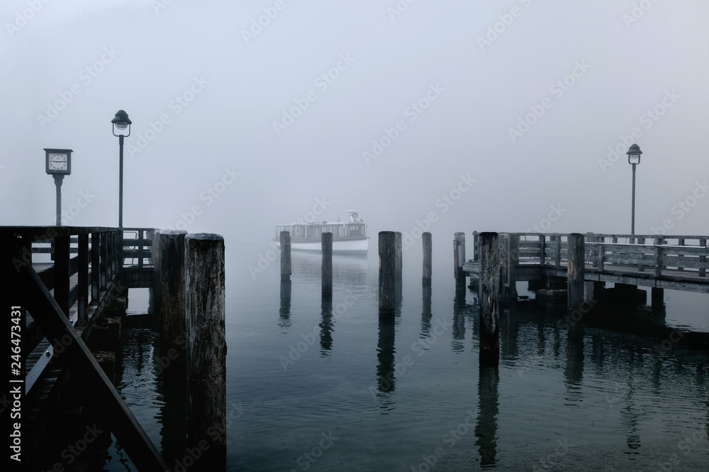 Views of the wooden pier in the mist and a lone boat on the Konigsee lake of Germany.