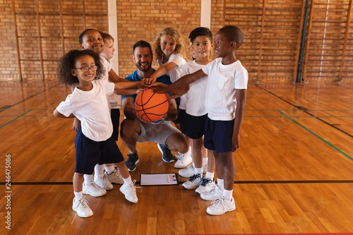 Schoolkids and basketball coach forming hand stack and looking