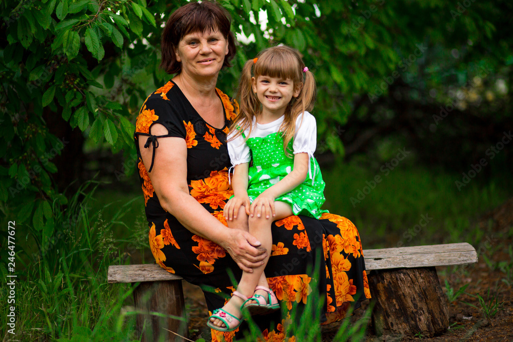Fototapeta premium Happy grandmother and little granddaughter sitting in summer