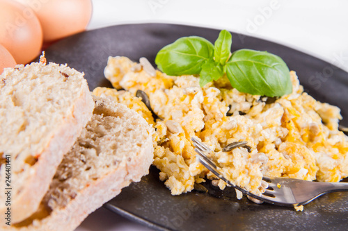Scrambled eggs with sunflower and pumpkin seeds, some fresh eggs and wholemeal bread, eaten with a fork, decorated with basil, on a white background