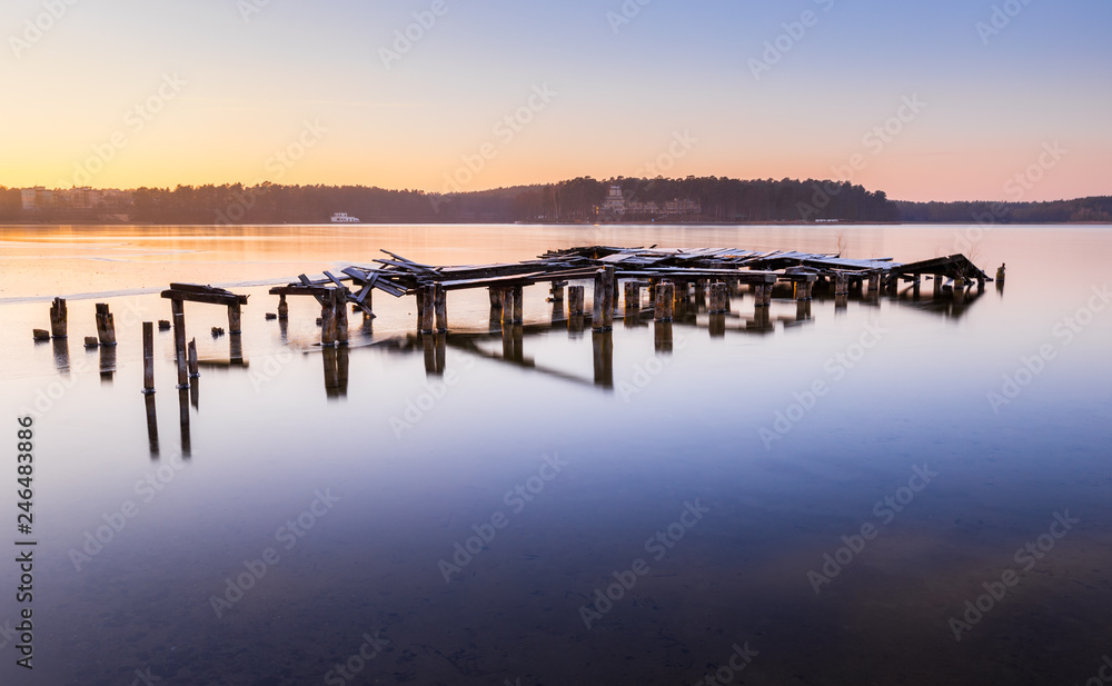 Destroyed bridge on the lake during a beautiful winter sunset