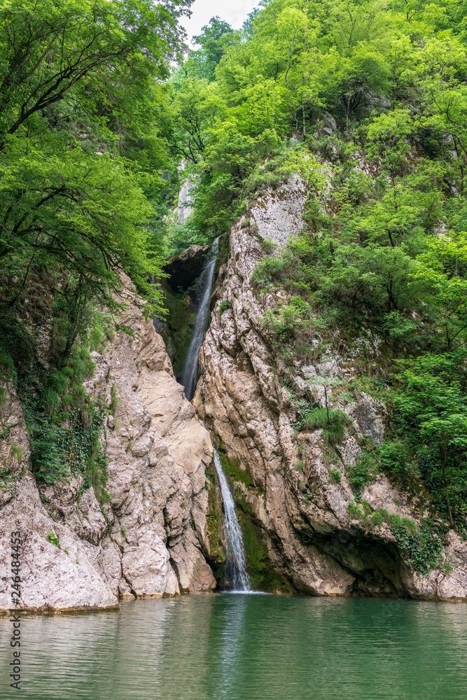 A high waterfall falls from a cliff into a clear lake A high waterfall falls from a cliff into a clear lake