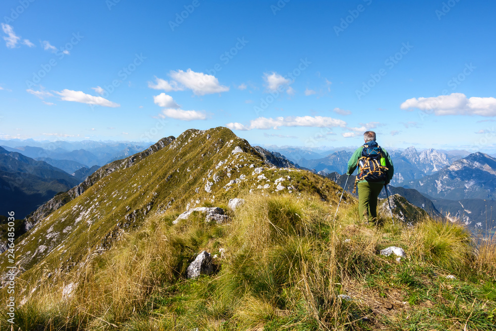 Man hiker walking on top of mountain against blue sky.