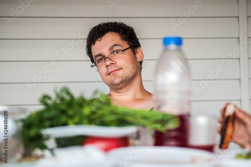 A young guy with glasses is sitting at the table with greens and healthy food photo